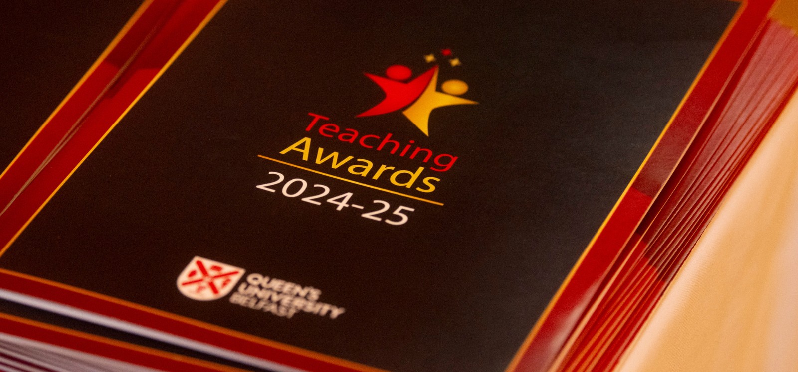 stack of Queens University Belfast Teaching Awards 2024-25 booklets resting on a table
