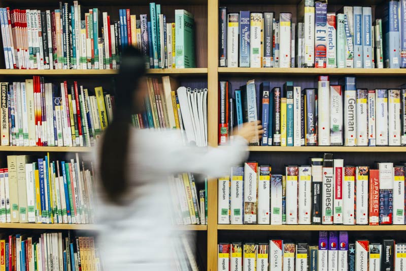 student removing a French language CD from a shelf of learning materials in the QUB Language centre