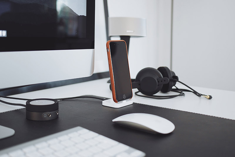 A white desk with a computer monitor, mobile phone and headphones on it