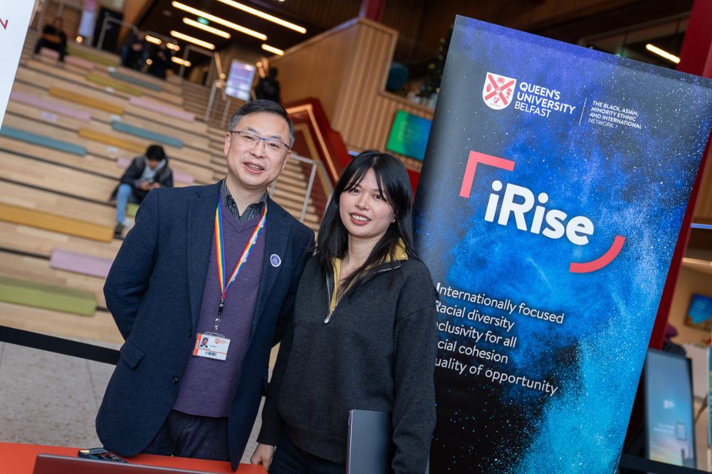 Two people stand smiling beside an iRise banner inside the Students’ Union, with tiered seating in the background.