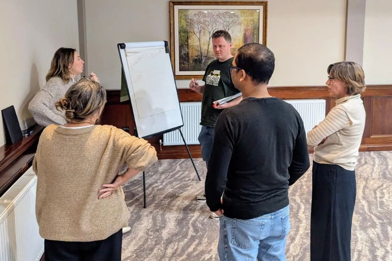 five people gathered in a room discussing something and noting ideas down on a flipchart
