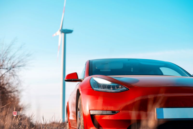 close-up of a red car parked in front of a wind turbine on a sunny day