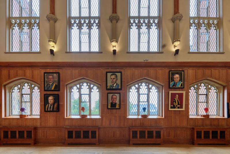six painted portraits hanging in an old, high-ceilinged hall, interspersing with eight arched windows