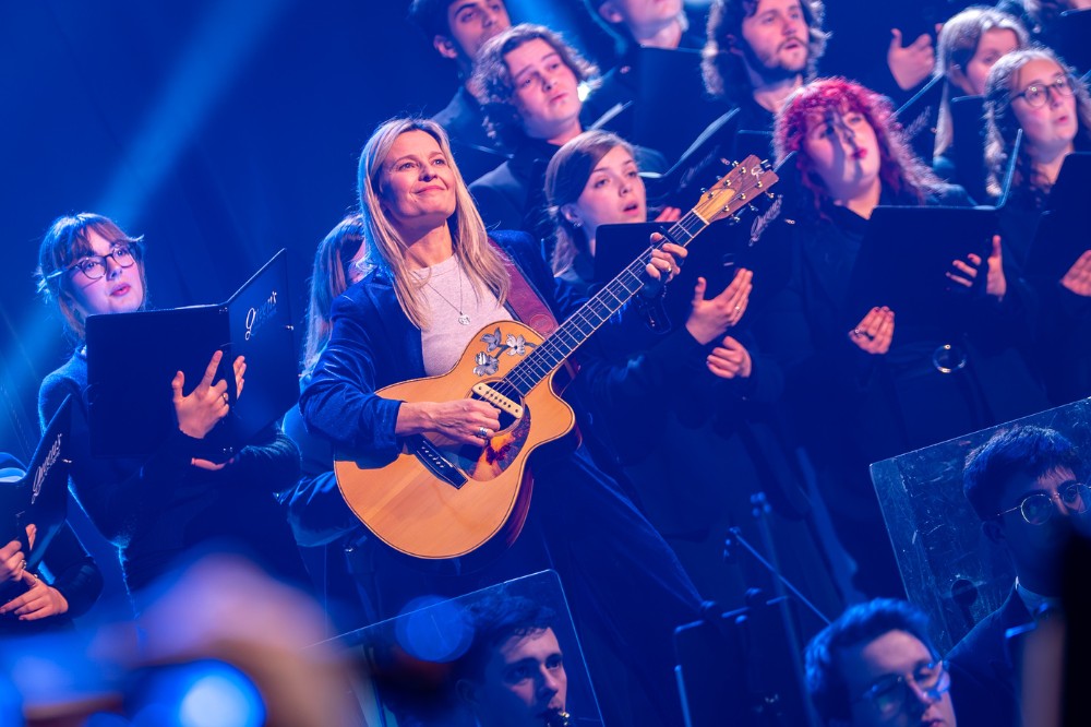 smiling woman playing acoustic guitar in front of a choir