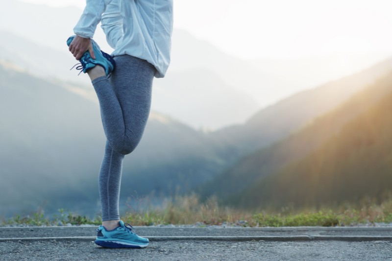 woman stretching before or during a morning/evening run, with mountains and valleys pictured in the background