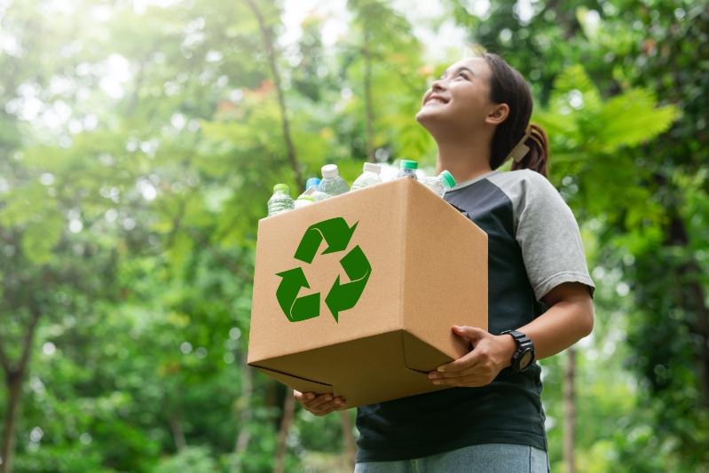 1. A woman holds a cardboard box featuring a recycling symbol, promoting eco-friendly practices and sustainability.