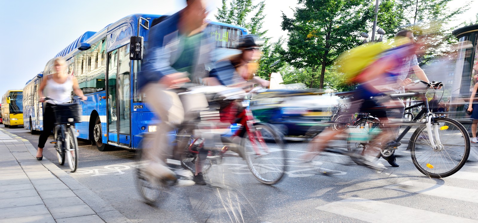 blurry, fast-moving people cycling on a busy road with buses and cars on a bright day