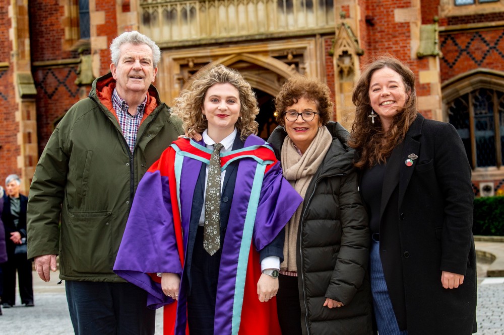 a young woman in graduation robe and her family and/or friends posing to camera in front of an old redbrick building